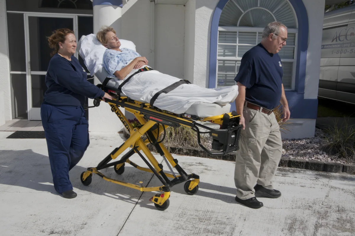 ACC Medlink crew wheeling a patient on a stretcher to the front door of a home