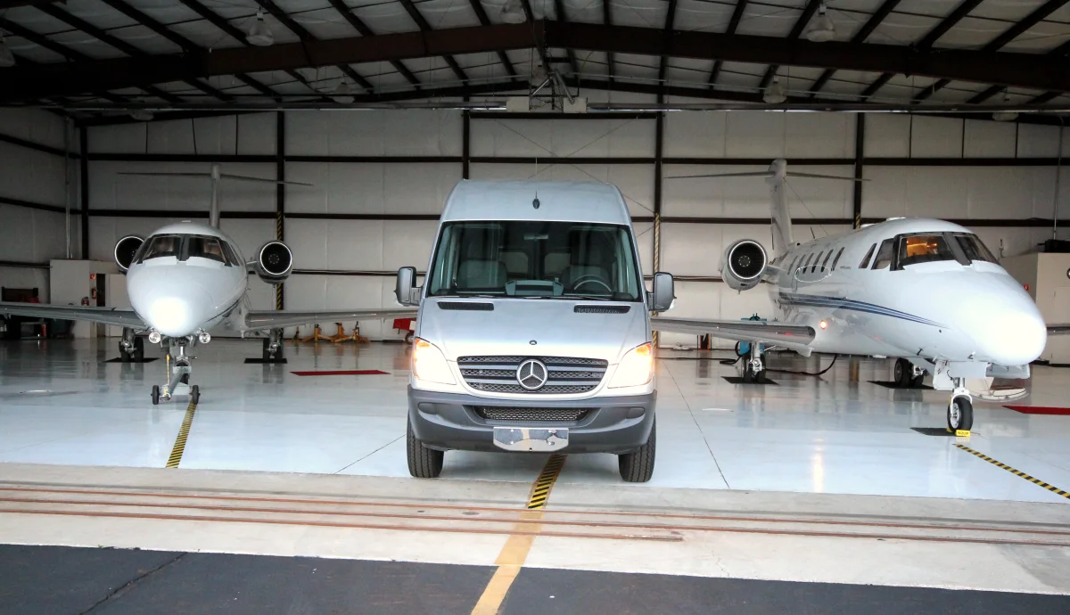 ACC Medlink Sprinter parked between two private jets in an aircraft hangar