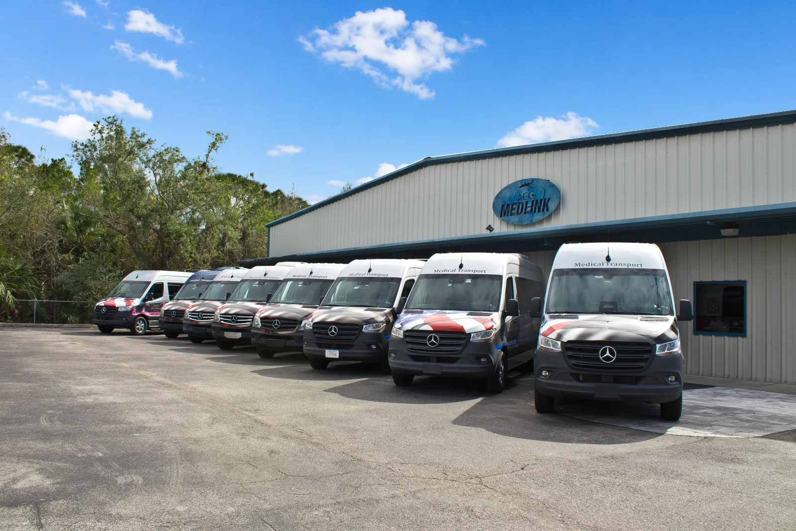 Row of ACC Medlink Mercedes Sprinter vans parked outside the company building