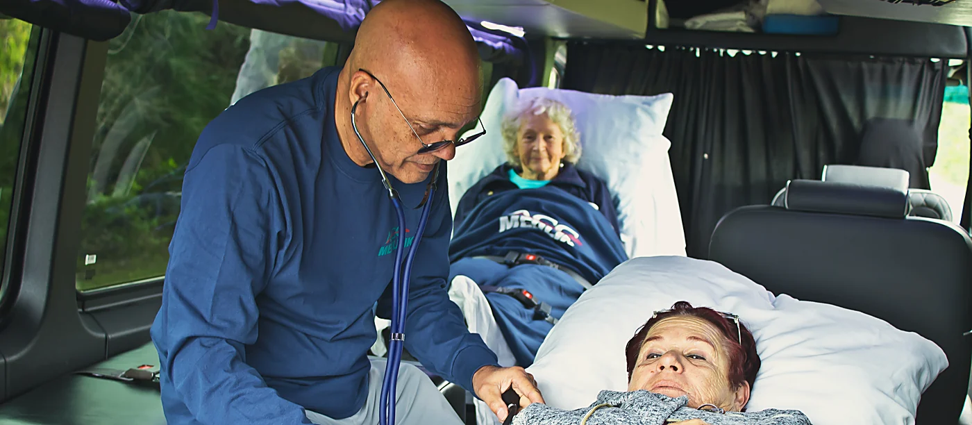 ACC Medlink medical professional gently checking on an elderly patient resting in a bed