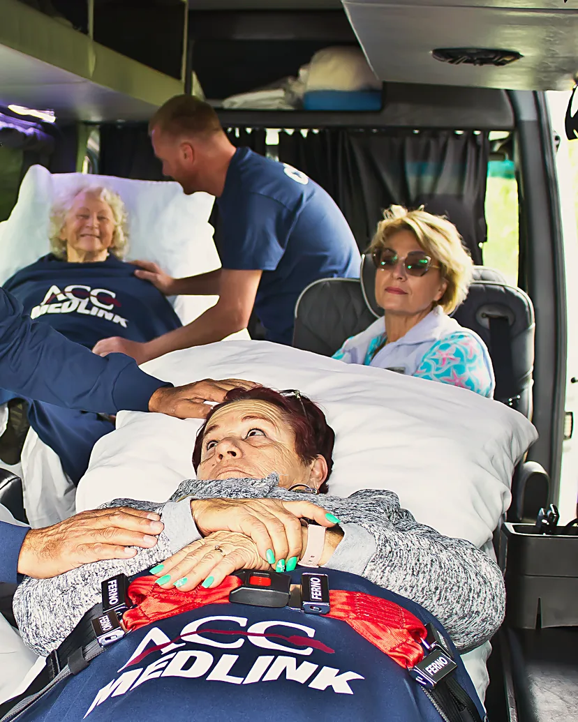 ACC Medlink attendant caring for a patient in a real bed while a family member rides in the seat beside her