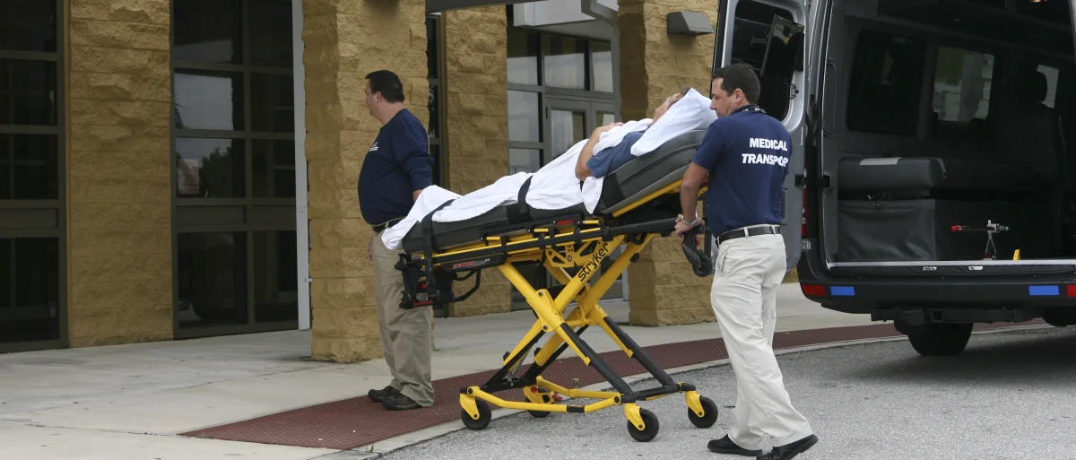 ACC Medlink crew wheeling a patient on a stretcher from a facility to the transport van