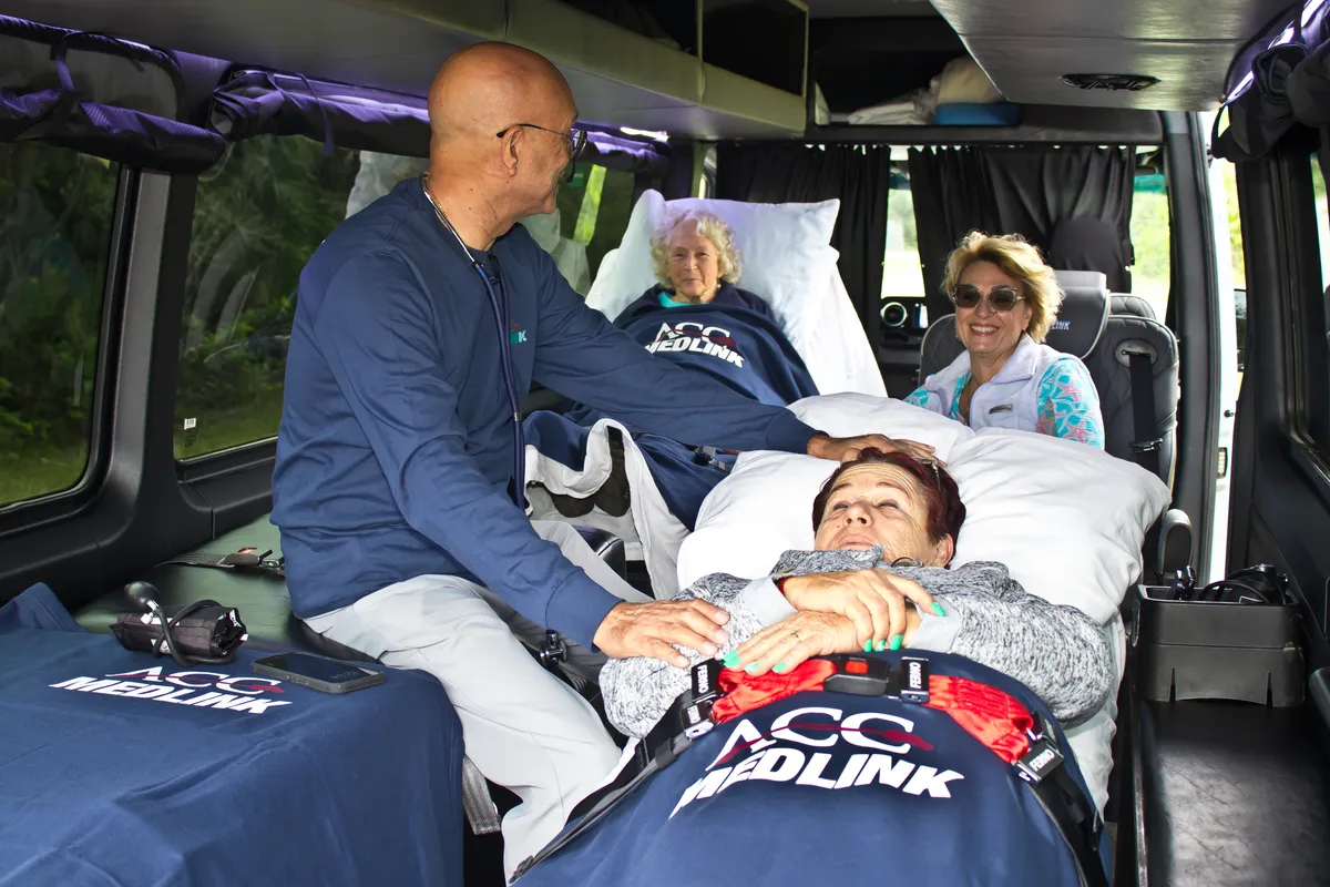 ACC Medlink medical attendant caring for two patients on beds inside a Sprinter while a family member rides along