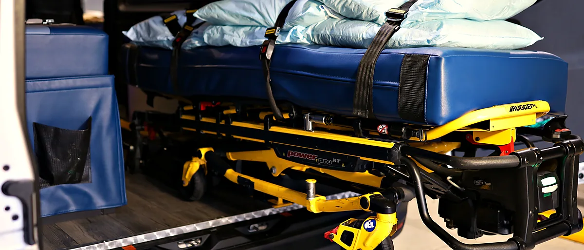 Power stretcher with a wide padded mattress loaded inside an ACC Medlink transport van