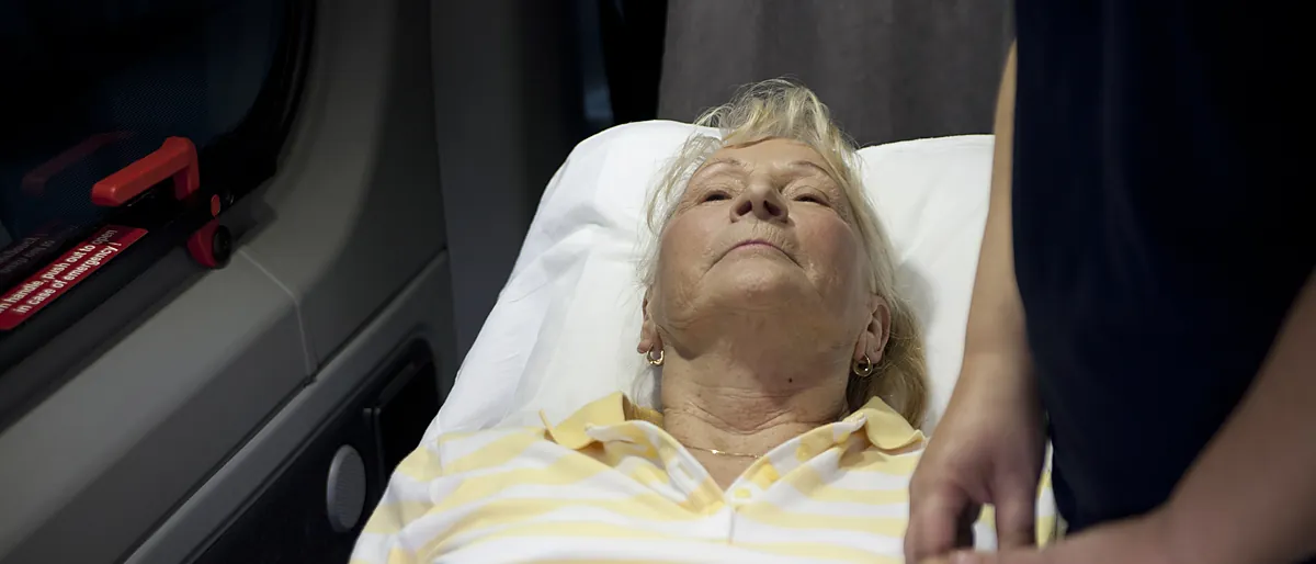 ACC Medlink attendant caring for an elderly patient in a real bed inside a transport van