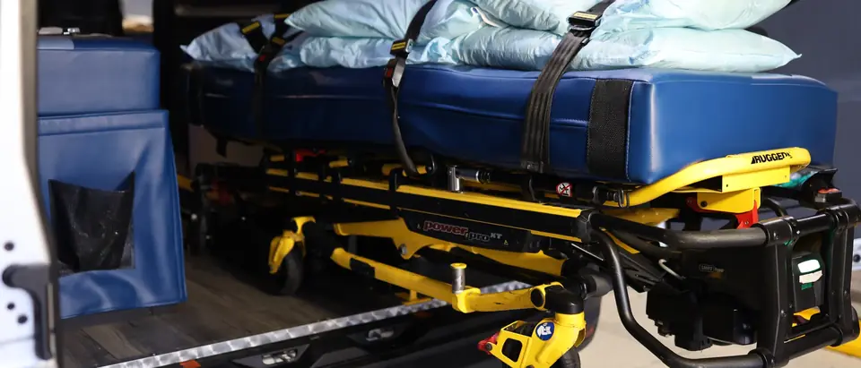Power stretcher with a wide padded mattress loaded inside an ACC Medlink transport van