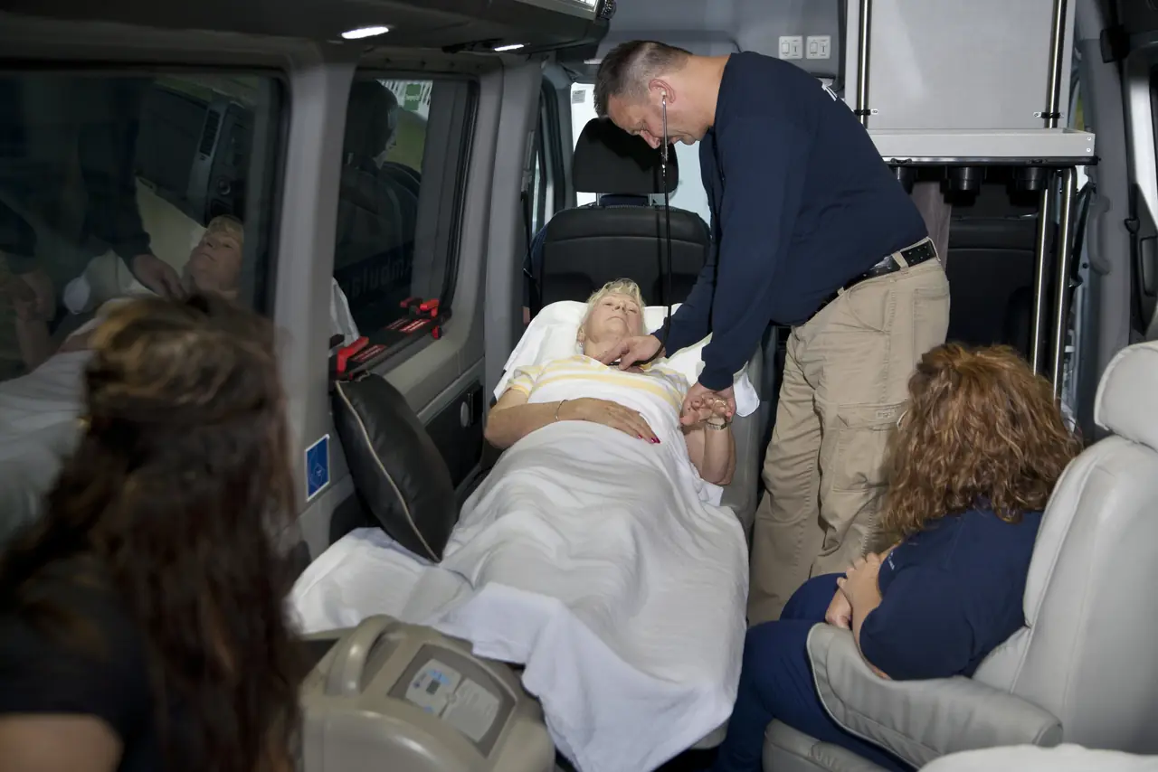 ACC Medlink crew member checking on a patient in bed inside the van as family sits nearby