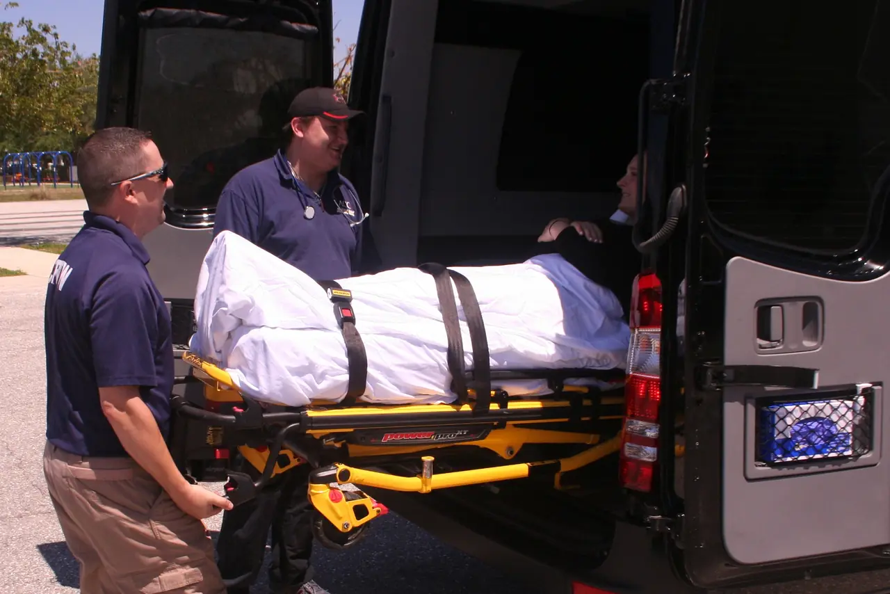 ACC Medlink crew loading a patient on a stretcher through the rear doors of a van
